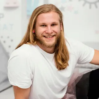 Junger Mann mit langen Haaren lächelt in einer Praxis