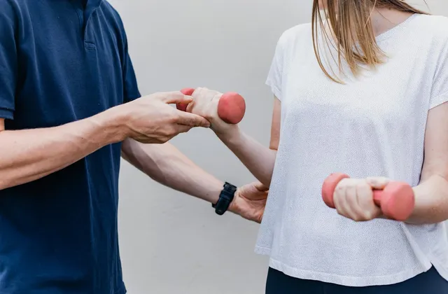 Physiotherapeut leitet eine Frau bei einer Übung mit kleinen Hanteln an